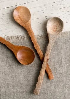 three wooden spoons and two wood spoons on a gray cloth with white background