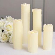 four white candles sitting next to each other on a table with flowers in the background