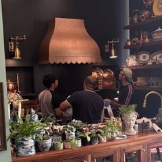 two men working behind the counter in a shop with potted plants and other items