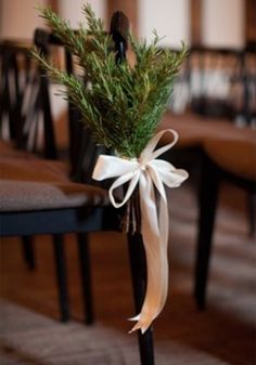 a white ribbon tied around a black chair with greenery on it's back