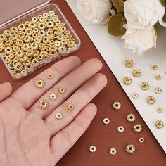 someone is holding their hand out to some gold colored beads in front of white flowers