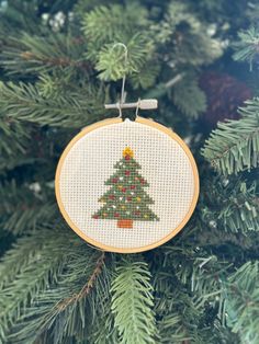 a cross stitch christmas tree ornament hanging from a pine tree