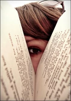 a person with glasses is peeking out from behind an open book that has words on it