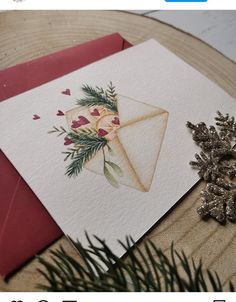 a christmas card with an envelope decorated with flowers and greenery next to pine cones