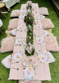 a long table set up with plates and place settings on the grass for a tea party