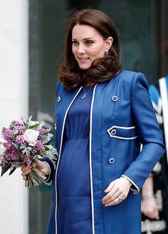 the pregnant woman is wearing a blue coat and holding a bouquet in her hand as she walks