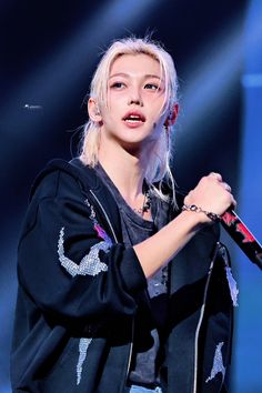 a woman with blonde hair and piercings on her arm holding a microphone while standing in front of a stage