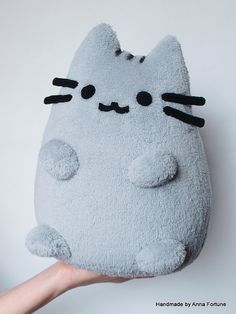 a hand holding up a gray cat shaped pillow with black eyes and nose on it