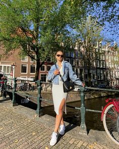 a woman standing on a bridge next to a bike and trees in the background,