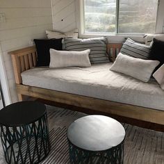 a couch with pillows on it in front of a window and two stools next to it