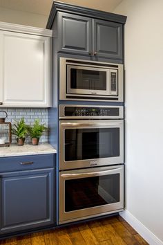 a kitchen with blue cabinets and stainless steel ovens, white cupboards, and wood flooring