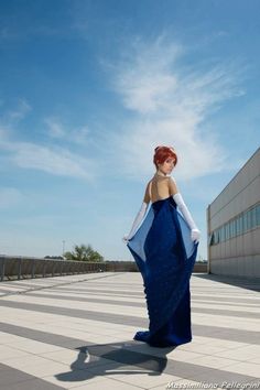 a woman in a long blue dress is standing on the ground with her hands behind her back