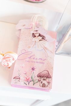 a pink birthday card with a fairy on it next to some cookies and cupcakes