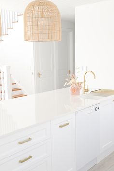 a kitchen with white cabinets and gold handles on the countertop, along with a vase filled with flowers