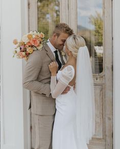 a bride and groom standing in front of a door with their arms around each other