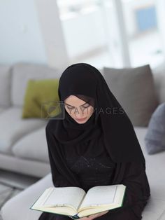 a woman sitting on a couch holding an open book in her hands and looking at the camera