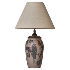 a lamp with a bird on it and a beige shade over the top that is sitting on a table