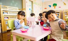 several children sitting at a table with bowls and plates on it in a classroom setting