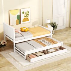 a white bed with drawers underneath it in a room next to a rug and pictures on the wall