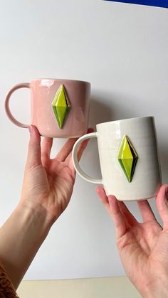 two women holding up mugs with green diamond decorations on the cups and one is pink