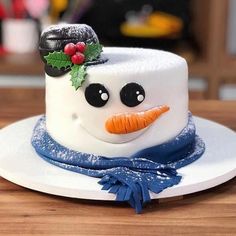 a snowman cake on a white plate with blue ribbon and holly berry decoration around the top