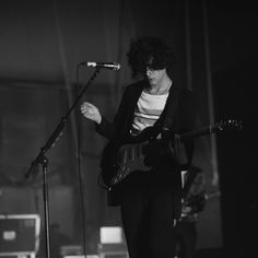 black and white photograph of a man playing guitar in front of microphones on stage