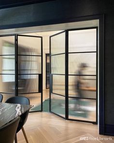 an open door leading to a dining room with black chairs and a marble top table