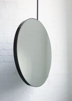 a round mirror hanging on the wall next to a brick wall with a metal hook