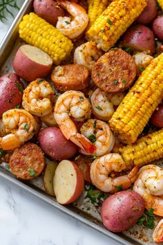 a tray filled with shrimp, potatoes and corn on the cob