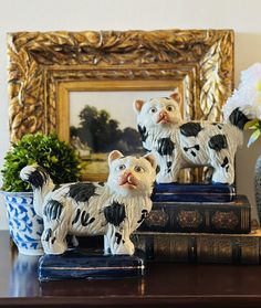 two ceramic cats sitting on top of books in front of a mirror and potted plant