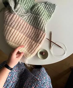 a knitted hat sitting on top of a table next to yarn and knitting needles