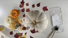 some pumpkins and leaves on a table with a paintbrush next to them in the process of being painted