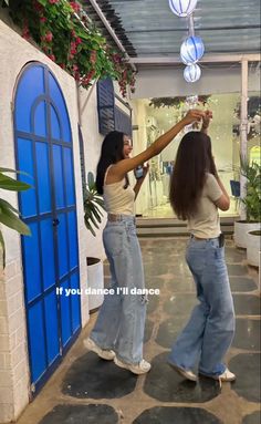 two women are dancing in front of a blue door