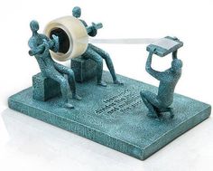 two figurines are holding up a roll of tape to each other as they stand on a stone base