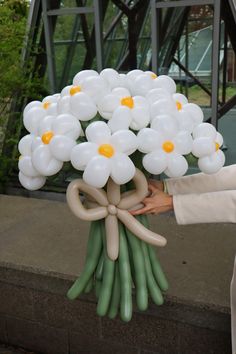 a bouquet of white flowers is being held by someone's hand with balloons attached to it