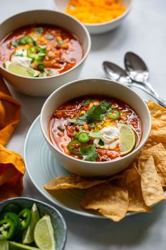 two bowls of mexican soup with tortilla chips and limes on the side