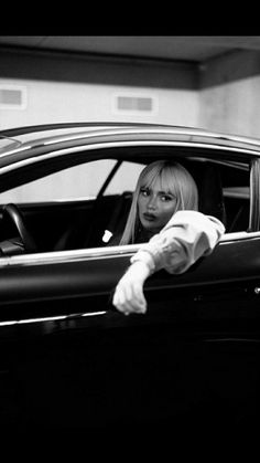 a woman sitting in the driver's seat of a car with her hand on the door handle