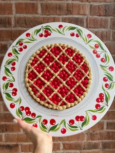 a hand holding a plate with a pie on it and cherries around the edge