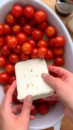 two hands holding a block of cheese and cherry tomatoes in a white bowl on a wooden table