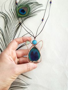 a person holding a piece of jewelry with peacock feathers on it and another bird's tail in the background