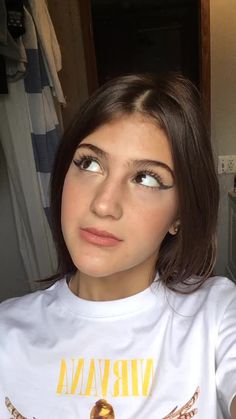 a woman with brown hair wearing a white t - shirt and looking at the camera