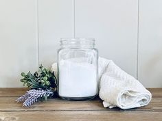 a glass jar filled with white sand next to a towel and lavender sprig