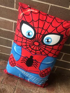 a bag with a spiderman face on it is sitting against a brick wall and has blue eyes