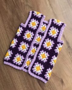 two purple and yellow crocheted squares with flowers on them sitting on a wooden surface