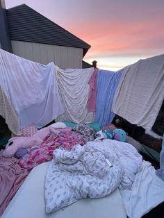 an unmade bed with clothes hanging from it's sides and on the ground