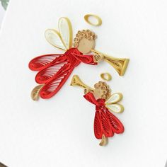 two red and gold angel brooches sitting on top of a piece of paper