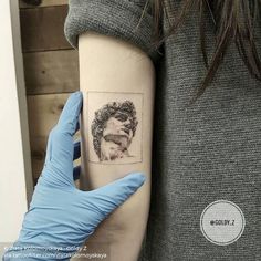 a person wearing blue gloves holding up a tattoo on their left arm with an image of a woman's face