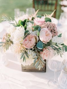 a vase filled with pink and white flowers sitting on top of a table next to wine glasses