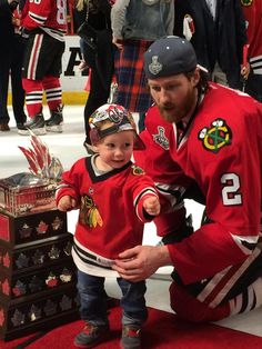 a man kneeling down next to a little boy wearing a hockey jersey and holding a trophy