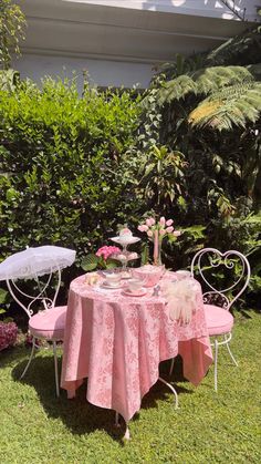 a pink table and chair set up for a tea party in the garden with flowers